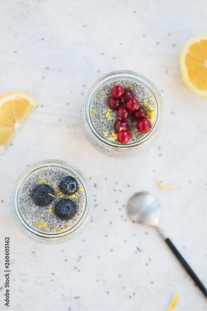 Top view of Jars of chia seed pudding made with chia seeds and almond milk and berries, goose berries, blueberries, lemon zests,  shallow depth of field, copy space and light background. 