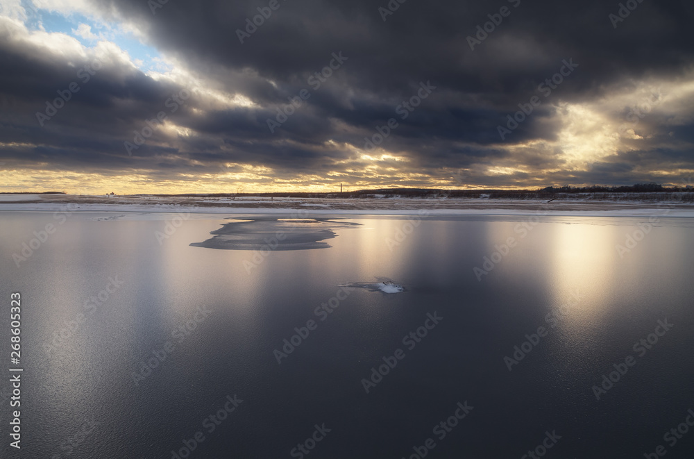 reflection of the stormy sunset sky in the icy surface of the river