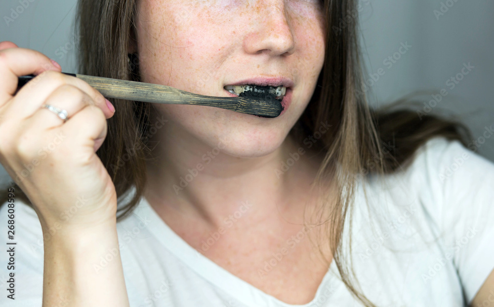 young woman brushing her teeth with a black tooth paste with active charcoal, and black tooth brush on white background for Teeth whitening young woman brushing her teeth with a black tooth paste with active charcoal, and black tooth brush on white background for Teeth whitening