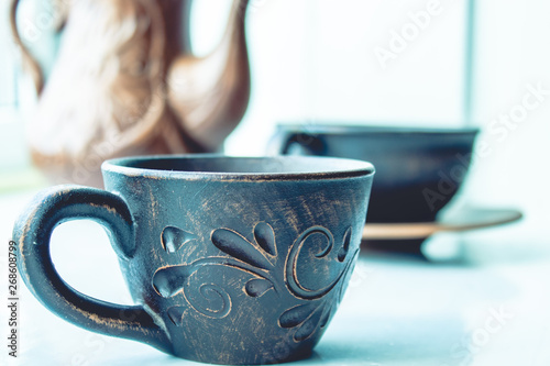 A teapot and a cup of clay are standing near the window.