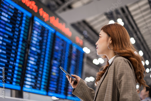 woman using smartphone with flight information board at airport