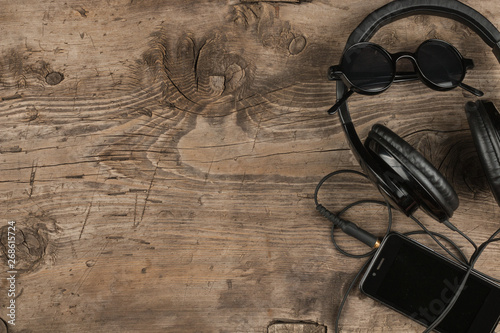 Top view. Black sunglasses, headphones and mobile phone on old wooden desk, vintage background.