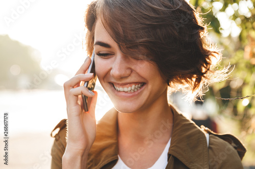 Cute young amazing woman walking outdoors in park in beautiful spring day talking by mobile phone.