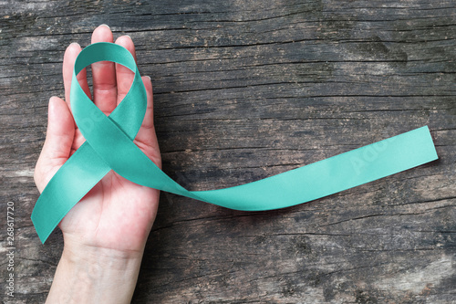Teal ribbon awareness on woman's hand for Ovarian Cancer, Polycystic Ovary Syndrome (PCOS) disease, Post Traumatic Stress Disorder (PTSD), Tourette's Syndrome, Obsessive Compulsive Disorder (OCD) photo