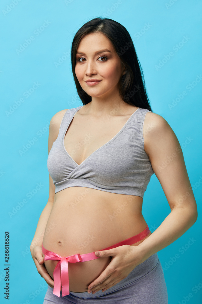 Bandage during pregnancy: how to choose and correctly wear it. Cropped image of beautiful pregnant woman with big exposed abdomen tied with pink ribbon Bandage during pregnancy: how to choose and correctly wear it. Cropped image of beautiful pregnant woman with big exposed abdomen tied with pink ribbon