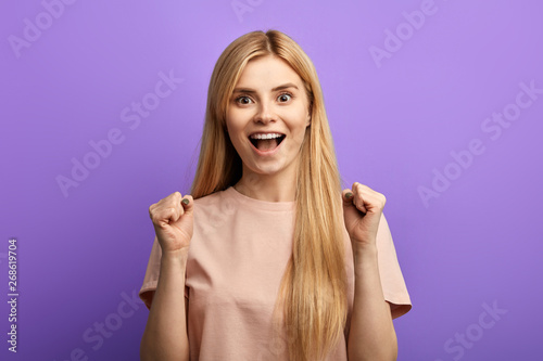 Happy positive successful blonde girl with raised hands shouting and celebrating success. isolated blue background. happiness, victory