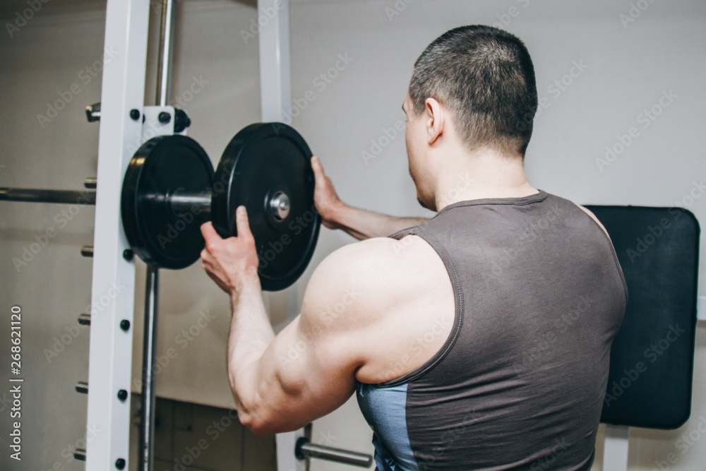 an athlete with big hands adds weight by the metal disks to the training apparatus in the training center. training equipment in the gym close-up an athlete with big hands adds weight by the metal disks to the training apparatus in the training center. training equipment in the gym close-up