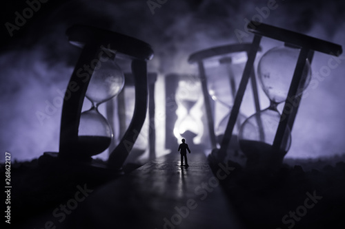 Time concept. Silhouette of a man standing between hourglasses with smoke and lights on a dark background. Surreal decorated picture © zef art
