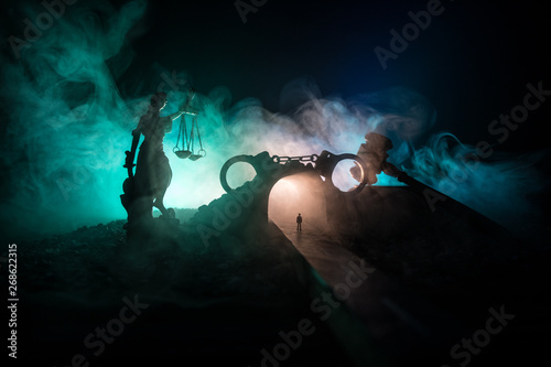 Legal law concept. Silhouette of handcuffs with The Statue of Justice on backside with the flashing red and blue police lights at foggy background. Selective focus