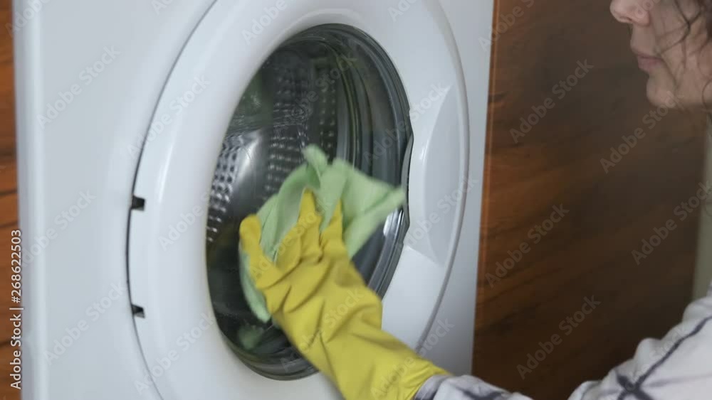 A woman cleaning a washing machine. A woman in protective gloves washes the door of a washing machine.