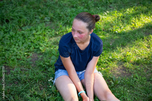 Portrait of a teen girl sitting on green grass in a park.