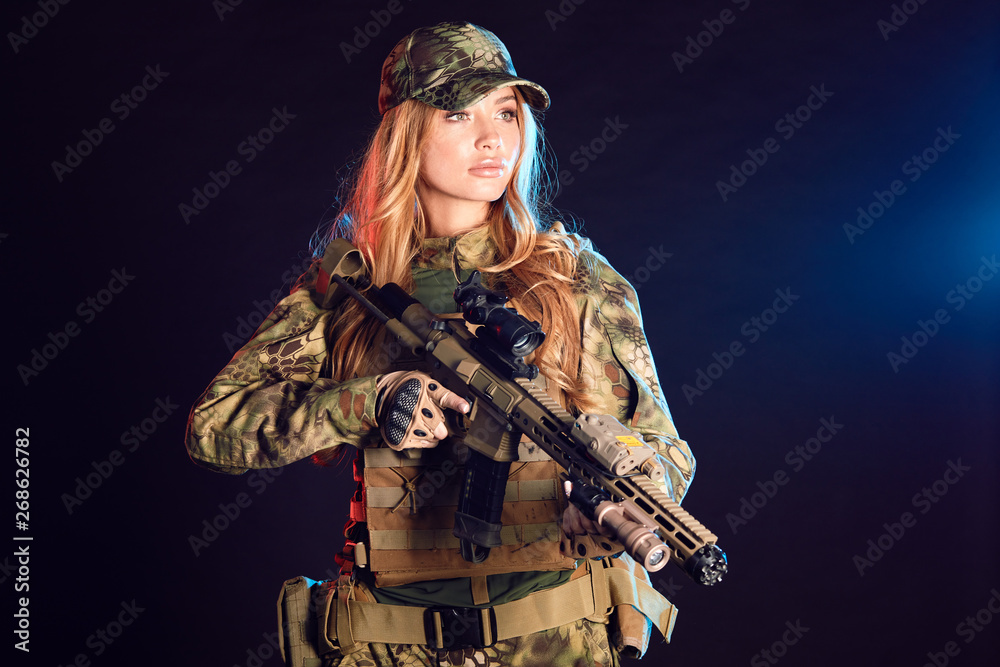 Sniper woman in ghillie suit, cap and plate carrier holds airsoft rifle over black background Sniper woman in ghillie suit, cap and plate carrier holds airsoft rifle over black background