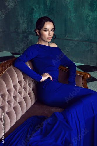 sexy young girl in long blue dress sitting on sofa in Studio with shabby walls