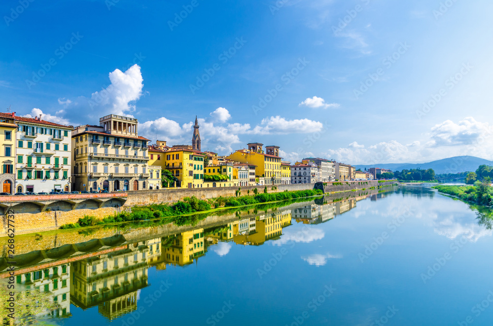 Arno River blue reflecting water and buildings on embankment promenade in historical centre of Florence city, blue sky white clouds, Tuscany, Italy