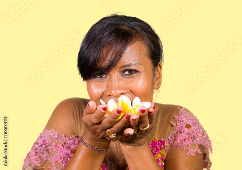 beautiful and happy middle aged Indonesian Balinese woman in traditional ceremony dress smiling and holding flower offering in her hands in welcome to Bali Hindu religion