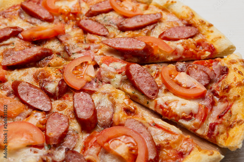 Italian pizza with smoked sausage slices and tomatoes, pizza cut, close-up Italian pizza with smoked sausage slices and tomatoes, pizza cut, close-up