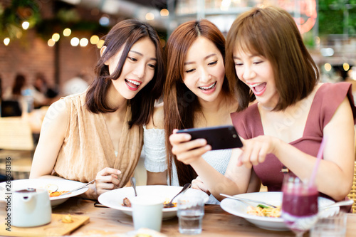 Happy friends having dinner and watching smart phone in  restaurant photo