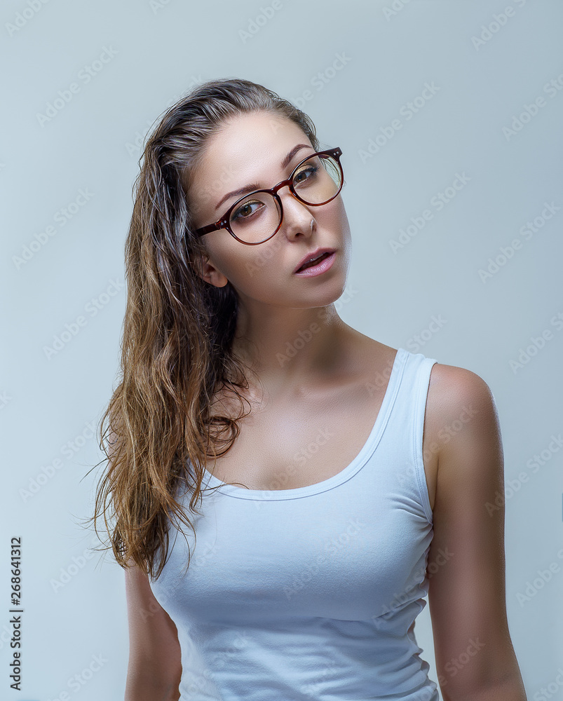 Woman in stylish glasses and white shirt is looking at the camera isolated on gray background in a studio close up. Fashion accessories photography with slim and sexy female model