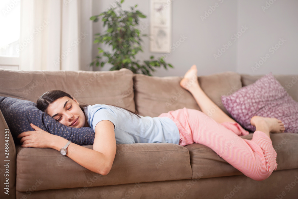 Tired funny young woman in summer everyday clothes stretches out and sleeps on sofa at home. Female student asleep in morning in living room after party, taking break for short sleep in middle of day  - obrazy, fototapety, plakaty 