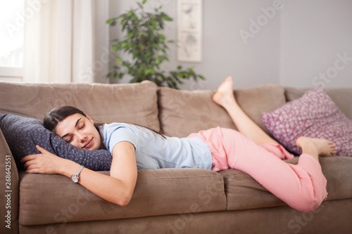 Tired funny young woman in summer everyday clothes stretches out and sleeps on sofa at home. Female student asleep in morning in living room after party, taking break for short sleep in middle of day 