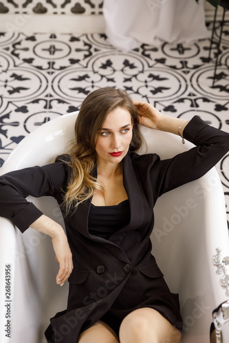 young beautiful blonde girl in stylish classic black clothes is sitting in the bathroom