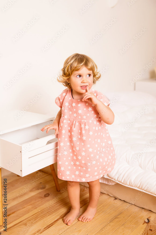 little beautiful girl in pink pajamas standing near the bed in the bedroom