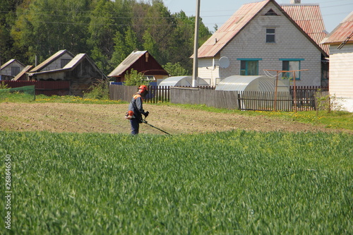 Lawn mower mows the grass on the edge of the field in the village on a Sunny summer day