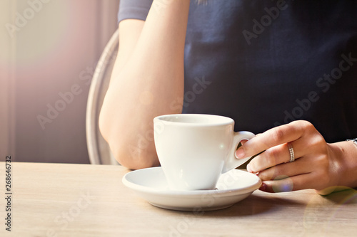 A cup of coffee in a cafe and a girl's hands.
