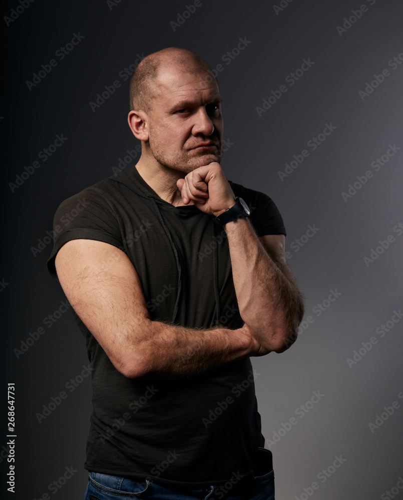 Sad angry crime man with bald head thinking with doubt look in agressive black shirt on dark grey background. Closeup Sad angry crime man with bald head thinking with doubt look in agressive black shirt on dark grey background. Closeup