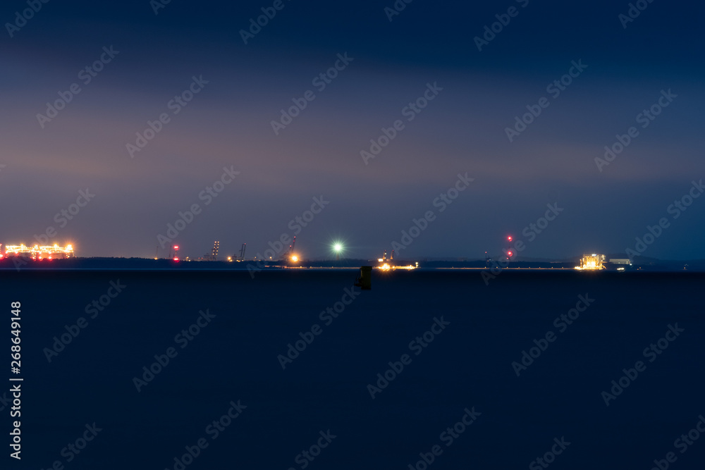 Mysterious lights of a distant port seen from a beach at night.