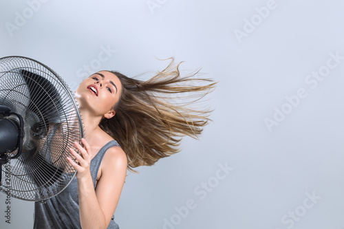 Foto Young woman enjoying cool wind from electric fan