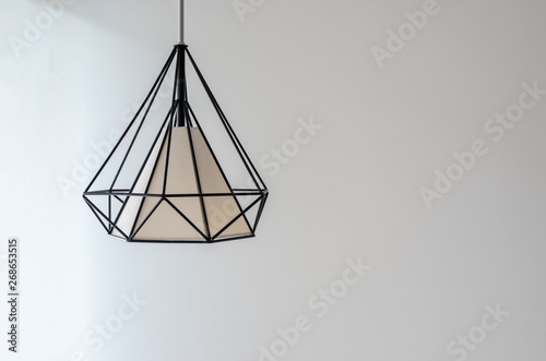 Modern lamp hanging down from ceiling on white wall background.