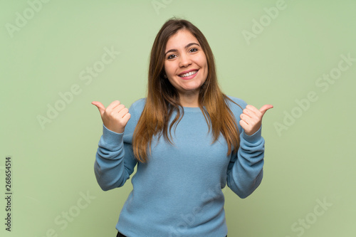 Young girl over green wall with thumbs up gesture and smiling