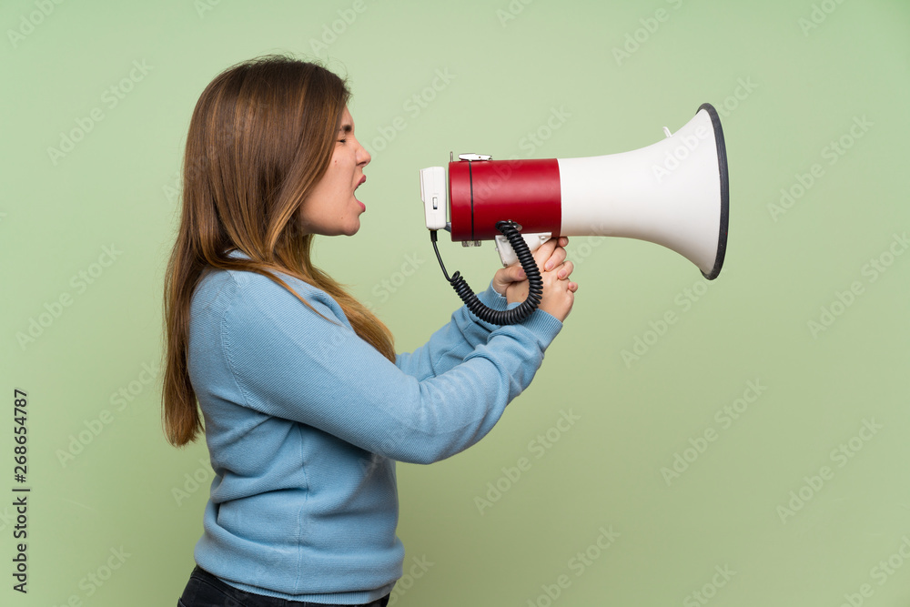 Young girl over green wall shouting through a megaphone Young girl over green wall shouting through a megaphone