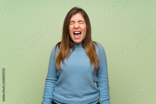 Young girl over green wall shouting to the front with mouth wide open