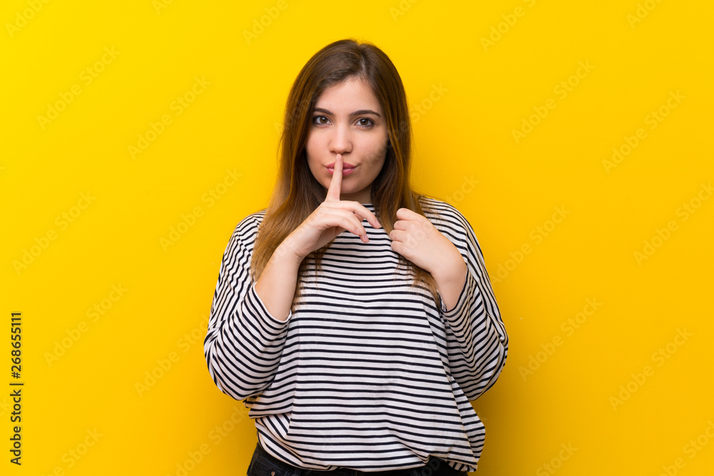 Young girl over yellow wall showing a sign of silence gesture putting finger in mouth Young girl over yellow wall showing a sign of silence gesture putting finger in mouth