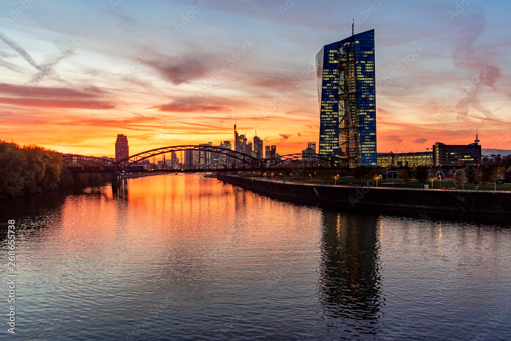 Europäische Zentralbank mit Frankfurter Skyline im Sonnenuntergang
