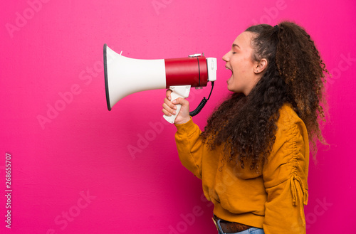 Teenager girl over pink wall shouting through a megaphone