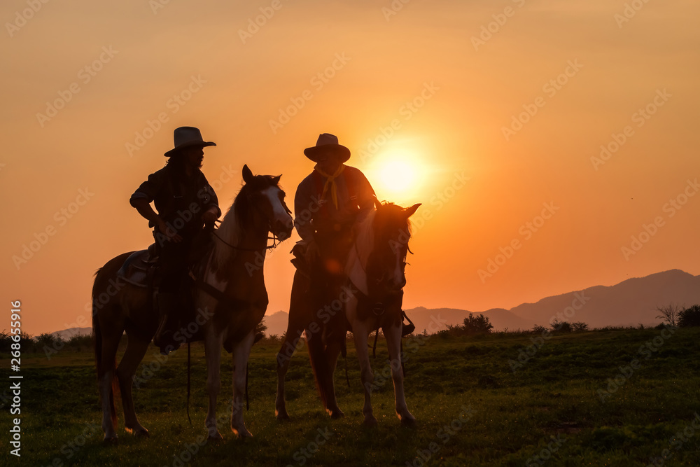 The silhouette of two men wearing a cowboy outfit with a horse and a gun held in the hand
