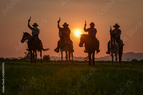 The silhouette of four men wearing a cowboy dress with horses and guns held in the hand.