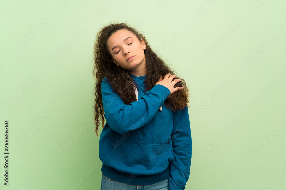 Teenager girl over green wall suffering from pain in shoulder for having made an effort