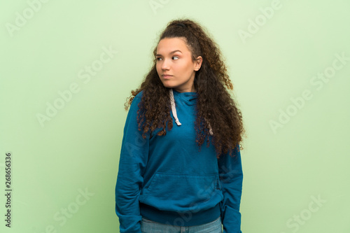Teenager girl over green wall making unimportant gesture