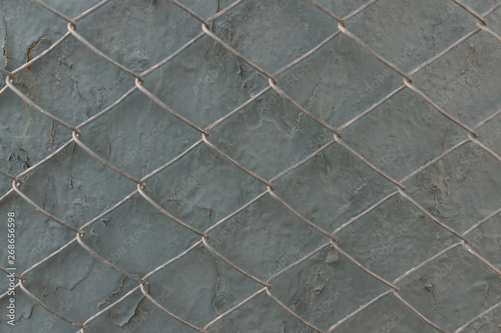 Fototapeta premium Metal grid on a gray wall with peeling paint. The concept of restriction of freedom.