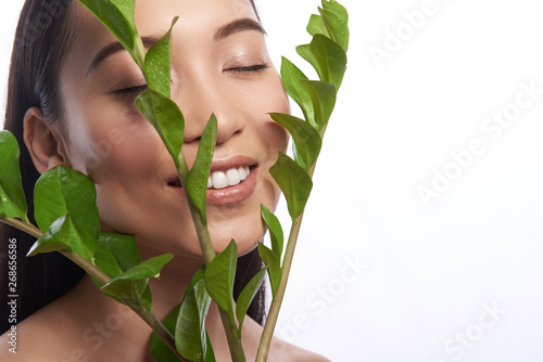 Peaceful Asian woman smiling and closing eyes while having branches