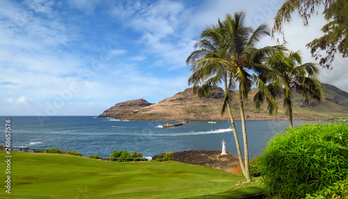 Scenic landscape of Kukii Point Lighthouse with palm trees, blue sea and sky, green golf course and mountains in the background, Kalapaki, Kauai, Hawaii, USA