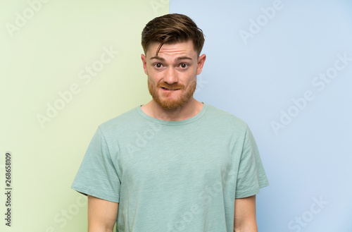 Redhead man over colorful background having doubts and with confuse face expression