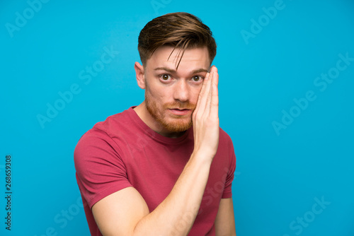 Redhead man on isolated blue wall whispering something