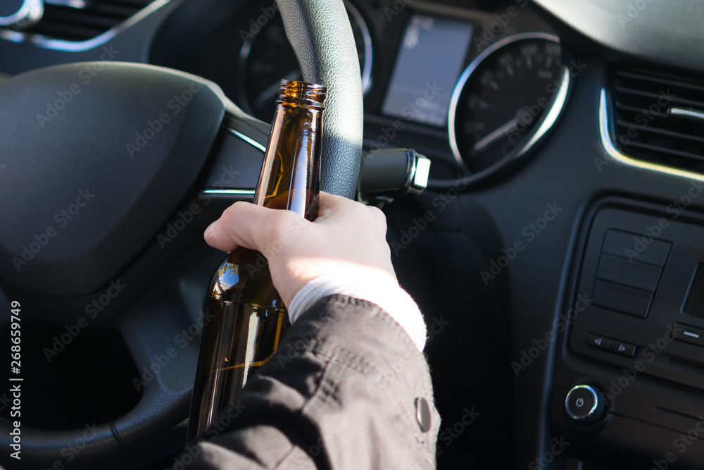 the driver behind the wheel of a car holds a bottle of alcohol in his hand the driver behind the wheel of a car holds a bottle of alcohol in his hand