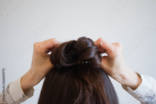 A young woman with brown hair ties her hair into a bun, viewed from the rear. Tutorial photo of simple hairstyle pinned half updo for long hair