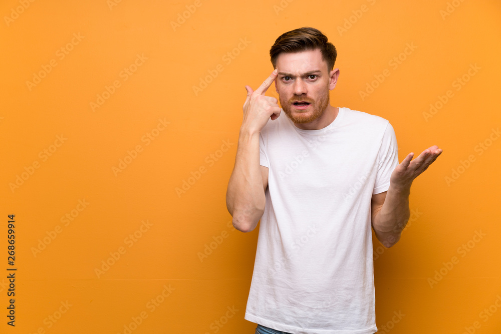 Redhead man over brown wall making the gesture of madness putting finger on the head Redhead man over brown wall making the gesture of madness putting finger on the head